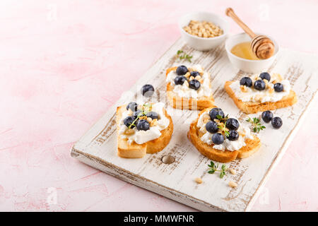 Toast Crostini mit frischen Beeren Heidelbeeren und Honig, Ricotta, Thymian und Haselnüsse, über weiß Holz- strukturierte Board. Ansicht von oben, kopieren. Stockfoto