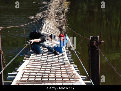 Die alte Brücke stürzt über den Fluss. Ein Mann hilft, eine gefallene Frau und reicht eine Hand. Stockfoto