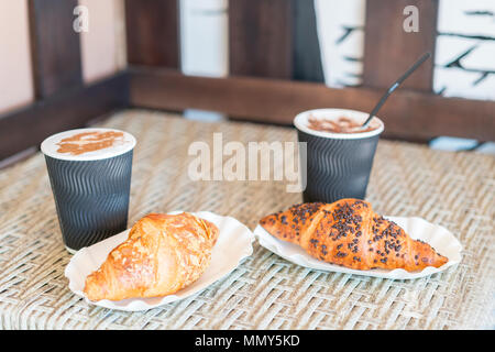 Cappuccino und Croissant. Zwei Tassen Kaffee mit Milchschaum steht auf einem Tisch in der Cafeteria. Zwei Tassen Kaffee und zwei Croissants auf der Straße in Cr Stockfoto