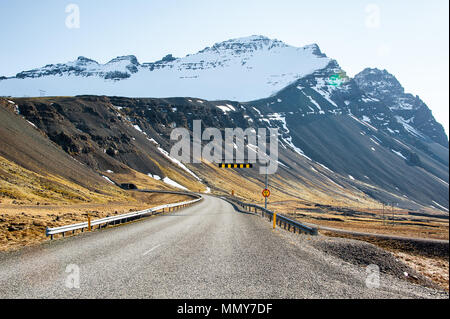 Route 1 (Ring Road) entlang der Ostfjorde, Island. Bunte Landschaft, schneebedeckte Berge, grasbewachsene Hänge und kurvenreiche Straße Stockfoto