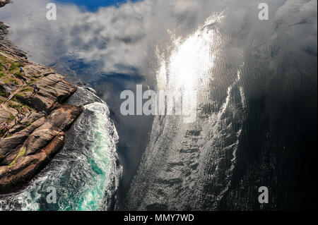 Blick auf den wirbelnden Ströme unter der Saltstraumen Brücke, Bodo, Norwegen. Sonnenlicht funkelt auf dunkelblauem Wasser, Cloud Reflexionen und felsigen Küste Stockfoto