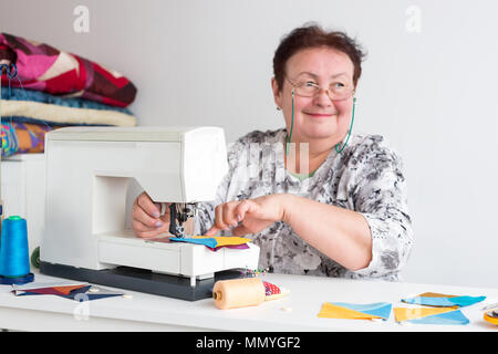 Technik, Handwerk, Beruf Konzept. Es ist ein altes lächelnde Frau Brille und weißem Hemd mit einer grauen florale Muster, sie sitzt Stockfoto