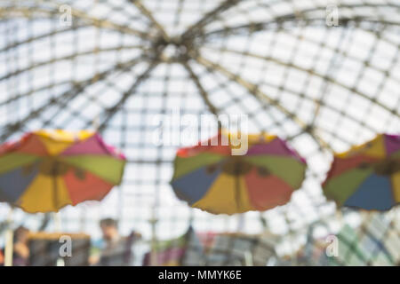 Nicht erkennbare Menschen ruhenden sitzen in Cafés unter hellen Sonnenschirmen am sonnigen Tag mit transparenten Dach. Urban modernen abstrakten Hintergrund. Verschwommen Effekt. Platz kopieren Stockfoto