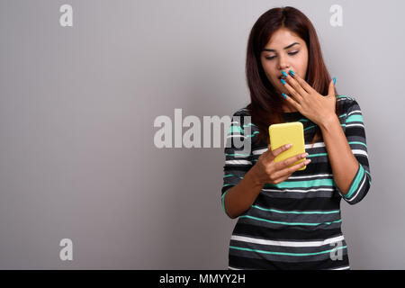 Junge schöne indische Frau mit Handy gegen Grau bac Stockfoto