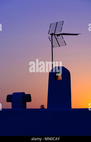 Analoge Antenne Silhouette am Dach bei Sonnenuntergang in gesättigtem Gelb, Rot und Blau Stockfoto