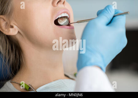 Erntegut Schuß von Mann in Handschuhe mit kleinen Mirror Tool und Kontrolle der Zähne der Frau im Zahnarztstuhl. Stockfoto