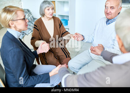 Ältere Patienten im Kreis sitzend mit Therapeuten und, Hände auf die Konsultation in betreutes Wohnen zu Hause. Stockfoto