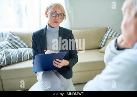 Erwachsene Frau in Gläsern Notizen auf Zwischenablage sprechen für ältere Menschen im betreuten Wohnen. Stockfoto