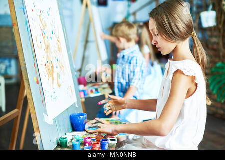 Seitenansicht Portrait von talentierten Teenager Malerei schönes Bild auf der Staffelei in der Kunst Klasse, mit anderen Kindern Stockfoto