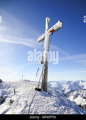 Gipfelkreuz mit Gebetsfahnen auf einem hohen Gipfel im Winter mit gefrorenen Eiskristallen auf dem Balken Stockfoto
