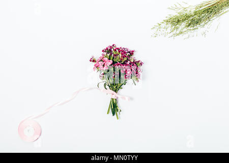 Ansicht von oben kleinen Blumenstrauß aus Sommer rosa Blüten mit wildes Gras und gebunden band. Flach florist Komposition. Stockfoto