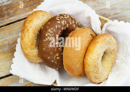 Auswahl an frisch gebackenen weißen, Sesam und braun Bagels im Brotkorb auf Holz- Oberfläche Stockfoto