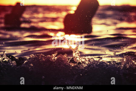 Brechende Welle zeigt ein Friedensabkommen unterzeichnen, während das goldene Sonnenlicht während der Sonnenuntergang über dem Strand auf Korsika widerspiegelt. Stockfoto