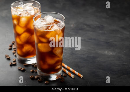 Eis Kaffee in einem großen Glas über und Kaffeebohnen auf einem alten rustikalen Holztisch. Kalten Sommer trinken auf einem dunklen Hintergrund mit Kopie Raum Stockfoto