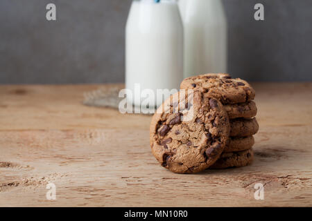 Ein Stapel von Cookies mit Milch Schokolade und zwei Flaschen Milch auf einem Holztisch Stockfoto