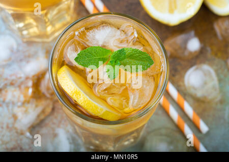 Traditionelle Eistee mit Zitrone, Minze und Eis in hohe Gläser. Ein Glas erfrischenden Sommer Drink auf der alten rostigen Hintergrund. Ansicht von oben Stockfoto