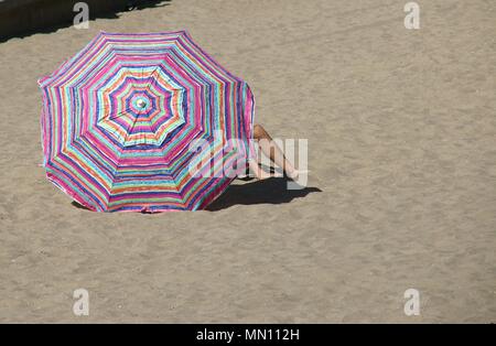 Mann, der sich unter einem Sonnenschirm, entspannend auf den Sand. Stockfoto