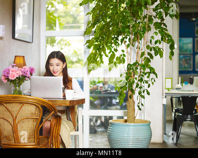 Schöne junge Asiatin im Café lesen Blogs mit Laptop. Stockfoto