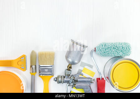 Verschiedene Werkzeuge auf weißem Holz- Hintergrund. Pinsel, Roller, Feldspritze, gelb und orange Farben Dosen, Farbmuster. Flach Stockfoto