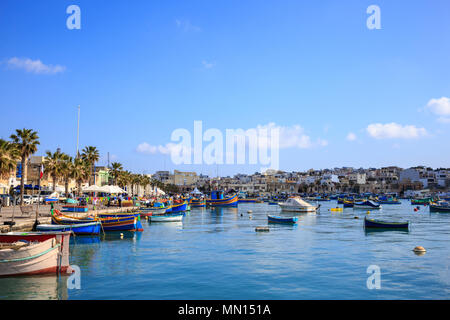 Marsaxlokk historischen Hafen voller Boote aus Holz in Malta. Blauer Himmel und Dorf Hintergrund. Ziel für Urlaub, Entspannung und Angeln. Stockfoto