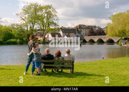 Bürgel, Hampshire, England, UK. Fluss Avon auf einem friedlichen Sonntagnachmittag. Ein Mann angeln in waders wird durch Diners in der Riverside Pub und Leute sitzen auf einer Bank im Park beobachtet. Stockfoto