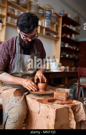 Porträt einer stattlichen bärtigen Mann Töpfer in Plaid Shirt und schmutzigen Schürze Arbeiten in seinem Atelier, selektiver Fokus, Nahaufnahme. Kreative Arbeit. Cra Stockfoto