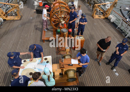 USCGC Eagle (WIX-327) ist eine 295 Fuß lange, dreimastige Barke, die 1936 in Deutschland gebaut wurde und 1946 als Trainingsschneider bei der United States Coast Guard in Betrieb genommen wurde. Das Archivbild dokumentiert Besatzungsmitglieder, die es einschifften Gästen, darunter Kinder der Gold Star Familie und Marinekadetten, erlauben, das Schiff zu steuern, während sie am 14. August 2017 im Atlantik unterwegs nach Baltimore sind. Stockfoto