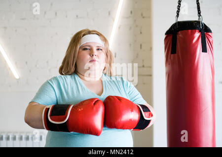 Taille bis Portrait von zuversichtlich beleibte Frau Boxhandschuh posiert mit Blick auf die Kamera bereit für extreme Training im Fitnessraum, Kopie Raum Stockfoto