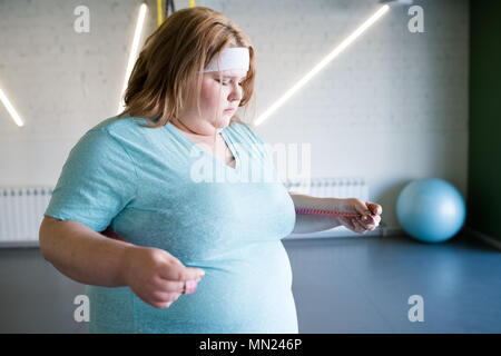 Taille bis Portrait von übergewichtige junge Frau messen Taille Größe nach weightloss trainieren Sie im Fitnessraum, kopieren Raum Stockfoto