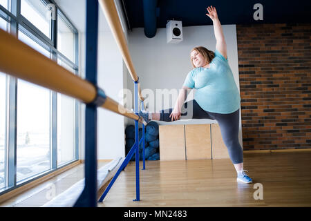 In voller Länge Porträt der übergewichtigen Jungen Frau, Ballett stellt sich bei gymnastischen Bar im Tanz Klasse, kopieren Raum Stockfoto