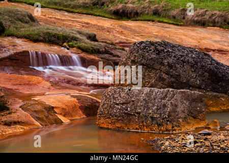 Ein kleiner Bergbach in Island laufen über Eisenhaltigen Felsen. Stockfoto