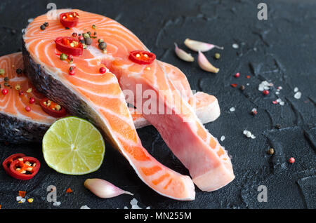 Zwei frischen, rohen Lachs Steaks mit Pfefferkörner, Chili, Salz, Zitrone und Knoblauch auf schwarzem Hintergrund. Gesunde Ernährung, Diät Konzept. Vorbereitung zum Kochen Stockfoto