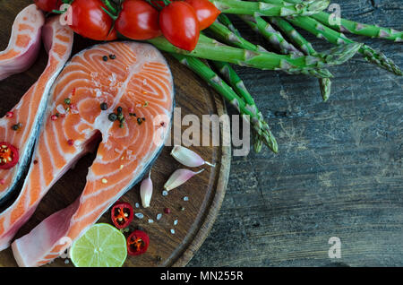 Zwei frash roher Lachs Steaks mit Gemüse und Gewürze: Spargel, Knoblauch, Tomaten, Pfefferkörner, Salz, Chili und Zitrone auf Holz Schneidebrett. Heilen Stockfoto