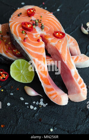 Zwei frischen, rohen Lachs Steaks mit Pfefferkörner, Chili, Salz, Zitrone und Knoblauch auf schwarzem Hintergrund. Gesunde Ernährung, Diät Konzept. Vorbereitung zum Kochen Stockfoto