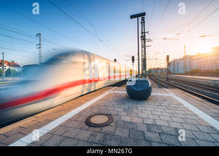 Weiße high speed Zug in Bewegung auf dem Bahnhof bei Sonnenuntergang. Deutschland. Verschwommen modernen Intercity Zug auf den Bahnsteig. Industrie. Passenge Stockfoto