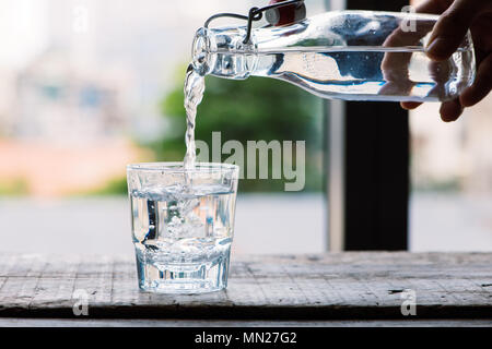 Sauberes Trinkwasser ist aus einer Kanne in einem runden Glas Schale goß auf einem Holztisch und ein hellgrün Serviette Nahaufnahme Makro auf eine grüne Natur Stockfoto