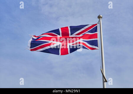 Union Jack Flagge in einer leichten Brise flattern auf einem Fahnenmast gegen einen hellblauen Himmel Stockfoto