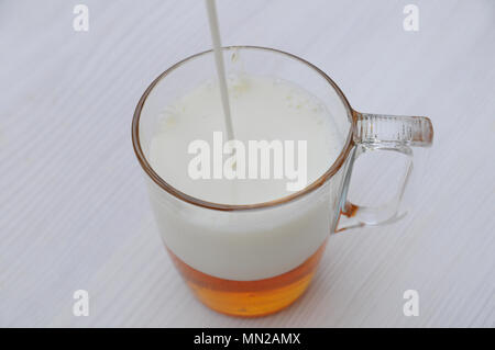 Gießen Milch im Glas mit Honig auf hölzernen Tisch Stockfoto