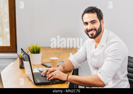 Dunkelhaarige Mann in Smart weißes Hemd mit der Eingabe auf Laptop, Konzept der Arbeitsatmosphäre im Büro Stockfoto