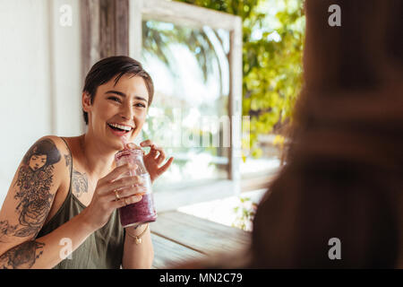 Frau mit einem Smoothie jar im Gespräch mit ihrer Freundin in einem Restaurant. Frau mit Tattoo auf der Hand in einem Restaurant Saft trinken. Stockfoto