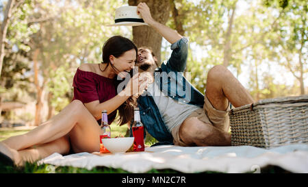 Paar auf einem Picknick im Park. Frau Lachen mit Mann spielt mit ihren Hut. Stockfoto