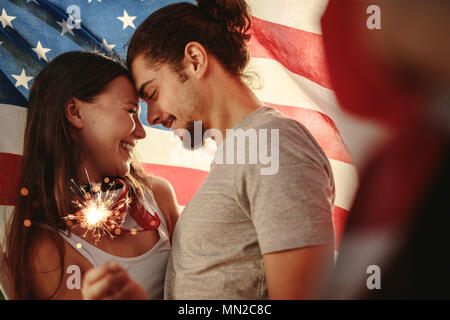 Liebende Paar hält Wunderkerzen unter amerikanischer Flagge umwickelt. Amerikanische Mann und Frau feiert Tag der Unabhängigkeit. Stockfoto