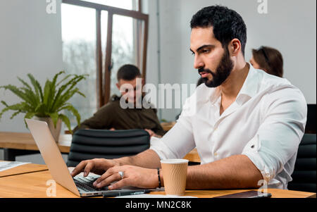 Attraktive bärtiger Mann im weißen Hemd arbeiten an Silber Laptop in modernen Büro Stockfoto