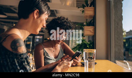 Zwei junge Frauen im Café sitzen können Sie über ihre Mobiltelefone. Weibliche Freunde social networking in einem Café. Stockfoto