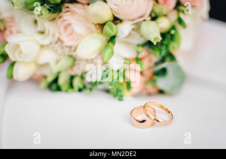 Trauringe liegen auf weisse Oberfläche gegen den Hintergrund der Blumenstrauß Stockfoto