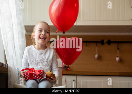 Cute Vorschüler Mädchen feiert 6. Geburtstag. Mädchen ihren Geburtstag Cupcake halten und schön verpackt, sitzt von Ballons umgeben. Stockfoto