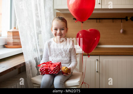 Cute Vorschüler Mädchen feiert 6. Geburtstag. Mädchen ihren Geburtstag Cupcake halten und schön verpackt, sitzt von Ballons umgeben. Stockfoto