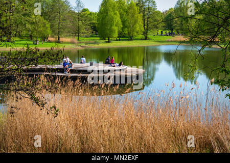 Britzer Garten, Neukölln, Berlin, Deutschland. 2018. Menschen entspannend auf die Holzterrasse auf der Insel im See im Frühjahr Stockfoto