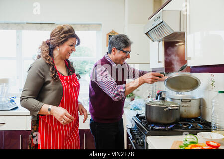 Reifes Paar kochen ein Curry zusammen in der Küche ihres Hauses. Sie werden lachen, während der Mann den Deckel vom Pan. Stockfoto