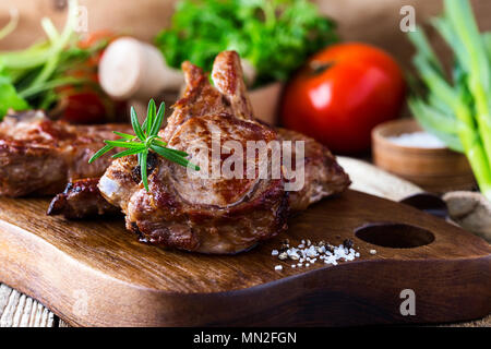 Gebratenen Kalbskoteletts mit frischen Kräutern und Gemüse auf rustikalen hölzernen Schneidebrett, in der Pfanne angebraten Steak zum Abendessen Stockfoto